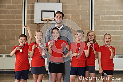 Victorious School Sports Team With Medals And Trophy In Gym Stock Photo