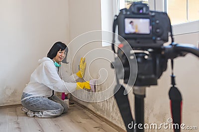 Video camera filming cheerful woman how removing mold from wall using spray bottle Stock Photo