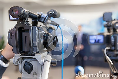 Video camera in focus, blurred spokesman in background Stock Photo