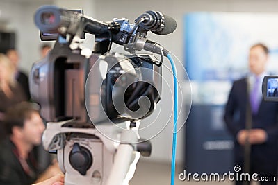 Video camera in focus, blurred spokesperson in background Stock Photo