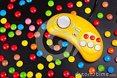 Video game console GamePad on a white wooden table. Yellow retro gamepad on a background of colored chocolate dragees. Stock Photo