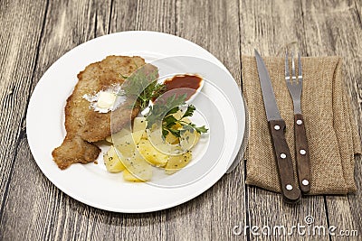 Vienna schnitzel with boiled potatoes for garnish on the plate . A dish on a plate on a wooden table with fork and knife. Photo fo Stock Photo