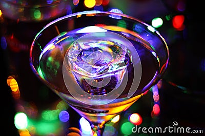 View on glass with martini cocktail with ice cube. Vibrant colorful bokeh background Editorial Stock Photo