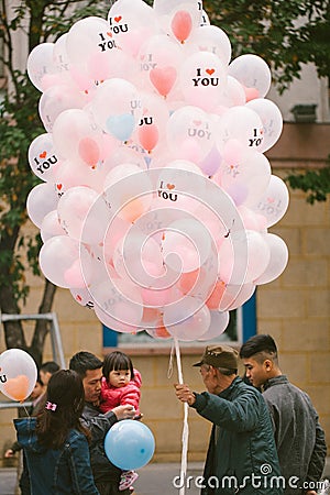 Vietnam. Hanoi. January 13, 2018 A balloon street vendor holding a bunch of balloons as a family walks over to buy one Editorial Stock Photo