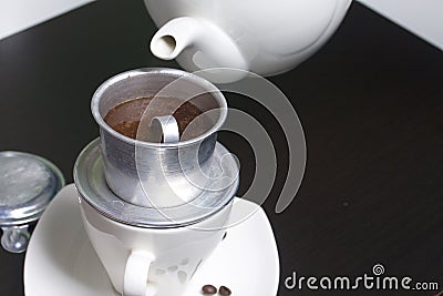 Vietnamese coffee maker is equipped on a cup. Ground coffee is poured into it. Barista pours boiling water from the teapot into it Stock Photo
