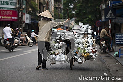 A vietnamese seller pushing her bike full of porcelain goods for sale in a street of Hanoi, Vietnam. Street Vendor on bicycle Editorial Stock Photo