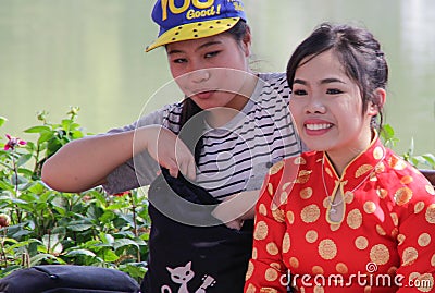 Vietnamese teenagers little girls in a traditional dress are sitting on a bench in the center of Hanoi Editorial Stock Photo