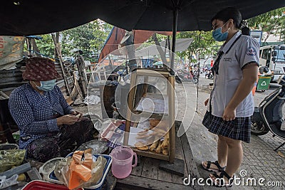 Vietnamese woman makes and sells snacks to a student in a street of Ho Chi Minh City Editorial Stock Photo