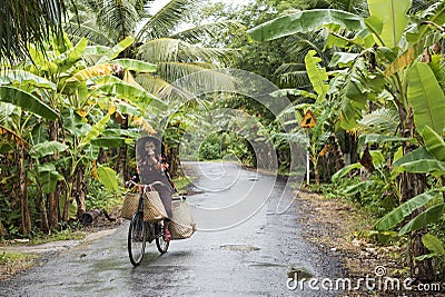 A Vietnamese woman rides her bicycle on a countryside road in the Mekong Delta. Editorial Stock Photo