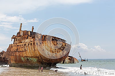 View of a abandoned ships carcasses in the ships cemetery, children bathing on the beach Editorial Stock Photo