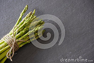 View from above of a bundle of green asparagus from above tied with twine on a gray slate counter with copy space Stock Photo