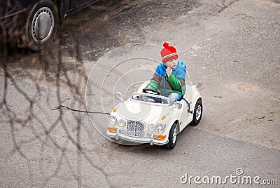 view from above, the child rides in children`s car, drives a car, a little boy in a red hat looks around Stock Photo