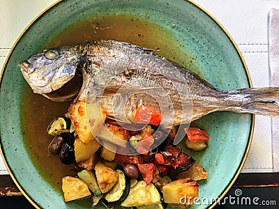 A view from above of a Delicious pan fried Mediterranean fish served on a plate with fresh vegetables at a restaurant Stock Photo