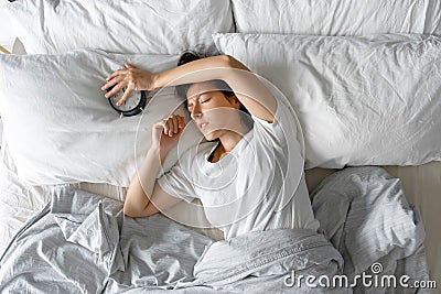 View from above. The girl sleeps next to the alarm clock. Trying to turn off the ringing alarm clock that interferes with sleep. Stock Photo