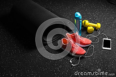 Top view of bright yellow dumbbells, a mat, bottle of water, sports shoes and phone on a black floor background. Stock Photo