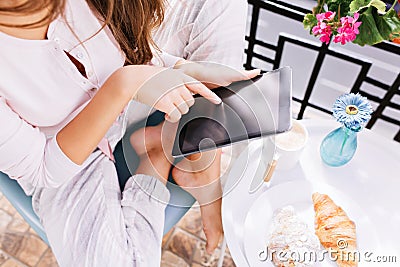 View from above tablet in hands of girl in pajama sitting on balcony, having breakfast. Stock Photo