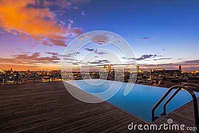 View across luxury roof top swimming pool to the city, with infinity edge, early morning sunrise, colorful sky in exotic Barcelona Stock Photo