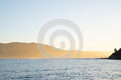 View across Tokomaru Bay in late afternoon as sun illuminates distant hills in golden glow above sea Stock Photo