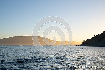 View across Tokomaru Bay in late afternoon as sun illuminates distant hills in golden glow Stock Photo