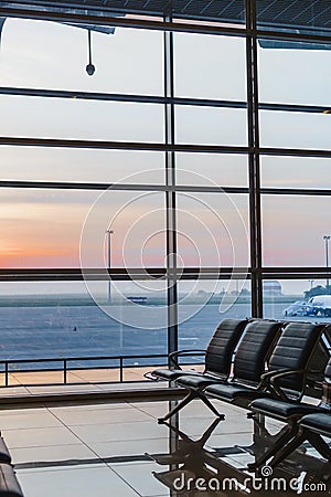 View of airport interoir, empty bench chairs in the departure hall during sunrise. Airplane and building background Stock Photo