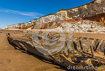 The carcass of a shipwreck on Old Hunstanton Beach beneath the white, red and orange stratified cliffs in Norfolk, UK Stock Photo