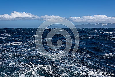 View of Atlantic Ocean and distant mountains, choppy water, calm blue sky with white clouds Stock Photo