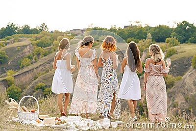 View from back. The company of gorgeous female friends enjoys a summer green hlls landscape and drink alcohol. People concept Stock Photo