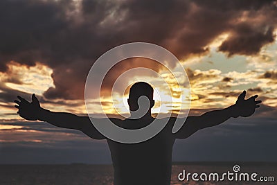 View from back of silhouette of athletic man with boxing gloves posing arms raised and biceps Stock Photo