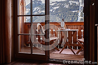 View through the balcony door to a cozy furnished balcony and a mountain slope with a ski lift and a forest area Stock Photo