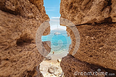 Bay in the Mediterranean with the yacht and the beaches through the rocks in the old ruined coastal fortress Stock Photo