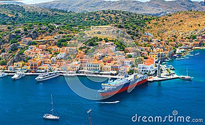 View on beautiful traditional Greek houses on Symi island green hills, yacht sea port, tourist ferryboat at Aegean Sea blue bay. M Stock Photo