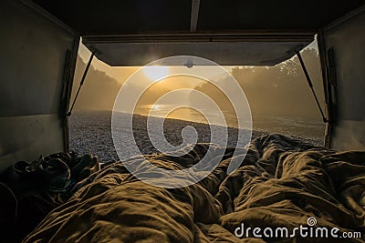 View from a bed in the vintage campervan parked on the shores of a river in early morning hours. Romantic overnight stay at a wild Stock Photo
