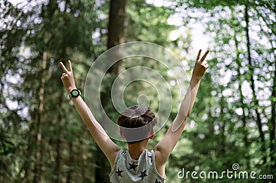 View from behind of a boy in his eary teens standing with his arms raised high in victorious gesture Stock Photo