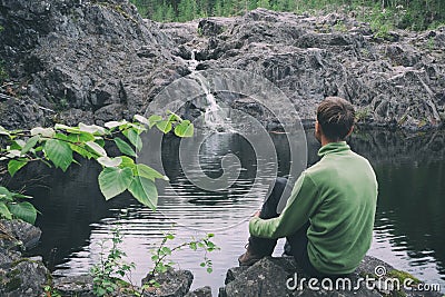 View from behind man hiker traveller sitting near mountain waterfall. Peaceful and calmness scenic view. Active person outdoor Stock Photo