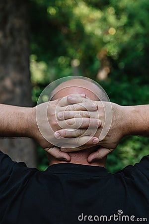 View from behind of mature man with little hair or alopecia with his hands on the nape of his neck. Stock Photo
