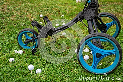 View of blue and black golf cart with three wheels, and white golf balls, on grass Stock Photo