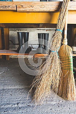 View of brooms and two pairs of rubber boots under a table in in a storage room Stock Photo