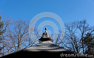 View of clear blue winter sky with decorative tiled pavilion roof and bare tree tops - with copy space in the sky Stock Photo