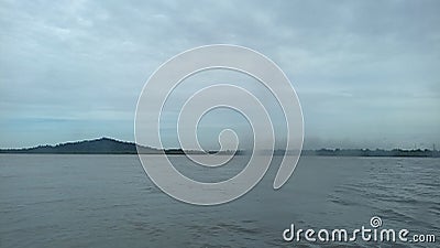 The view of a clear sky and a hill from atop a ship in the middle of the sea Stock Photo