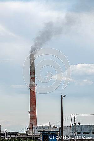 View of a complex of industrial buildings with smoking chimneys in the afternoon against the sky with clouds Stock Photo