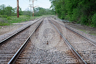 View of a double steel railroad tracks with trees on the side of the road Stock Photo