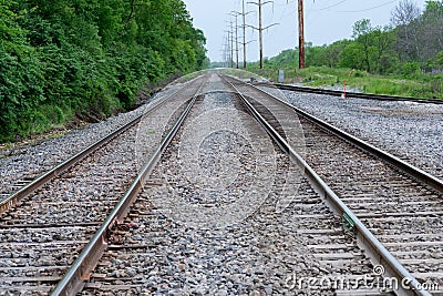 View of a double steel railroad tracks with trees on the side of the road Stock Photo