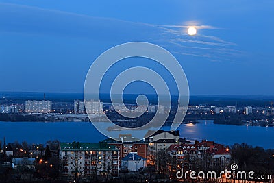 View of early moon in blue evening sky with reflection in the river. Cityscape Stock Photo