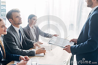 View of employee with clipboard standing near recruiters at table Stock Photo