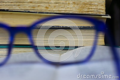 View through enlarging zoom lens of blue reading glasses on pile of antique yellowed books Stock Photo