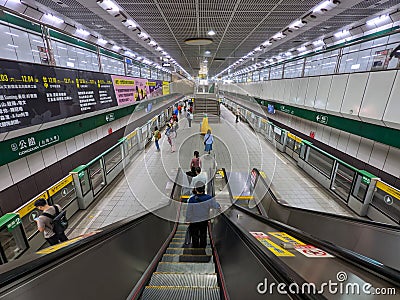 View from an escalator towards a two-way train platform with passengers waiting for trains in front of platform doors Editorial Stock Photo