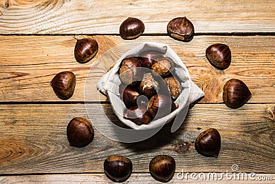 View of a fabric sack full of chestnuts surrounded by other chestnuts on a wooden background Stock Photo