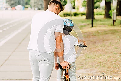 View of father helping son to ride on bicycle while kid sitting on bike Stock Photo