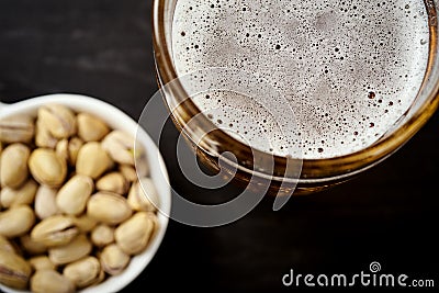 View of the foam of delicious beer in a glass and pistachios in a white bowl Stock Photo