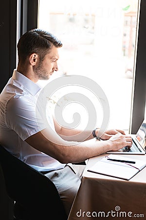 View of focused freelancer typing on laptop keyboard while sitting in cafe Stock Photo